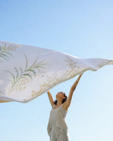 A luxury model holding up the Sovereign white and green floral Tencel luxury bedsheet against a bright blue sky, showcasing its lightweight, silky-smooth drape