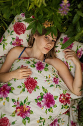 A lifestyle model resting under Couture white and fuchsia 500 thread count organic luxury bedsheet surrounded by vibrant flowers