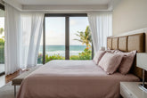 Full bedroom view displaying Hush luxury classic pink cotton bedsheet styled in an ocean-view bedroom with matching pillows and elegant tonal plaid design