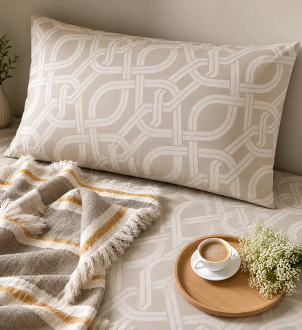 Chaste luxury beige cotton pillow cover on matching jacquard bedsheet, featuring an elegant interlocking geometric pattern and refined bedroom styling with a cup of tea showcasing lifestyle