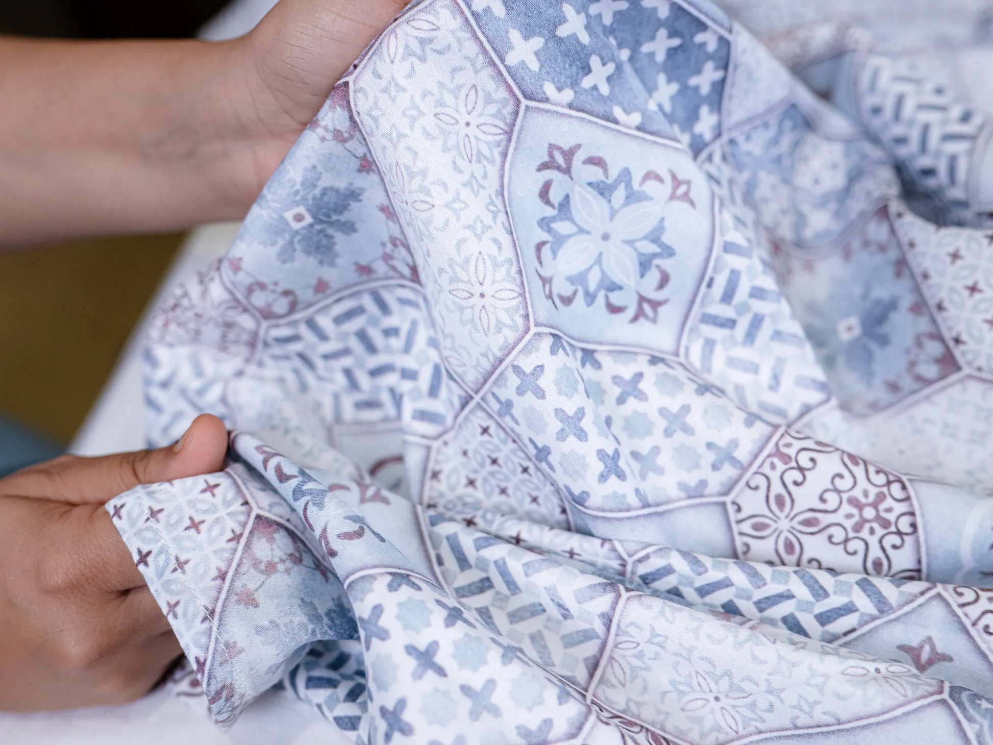 Handheld close-up of Echelon indigo blue cotton bedsheet highlighting smooth texture, skin-friendly finish, and elegant mosaic design