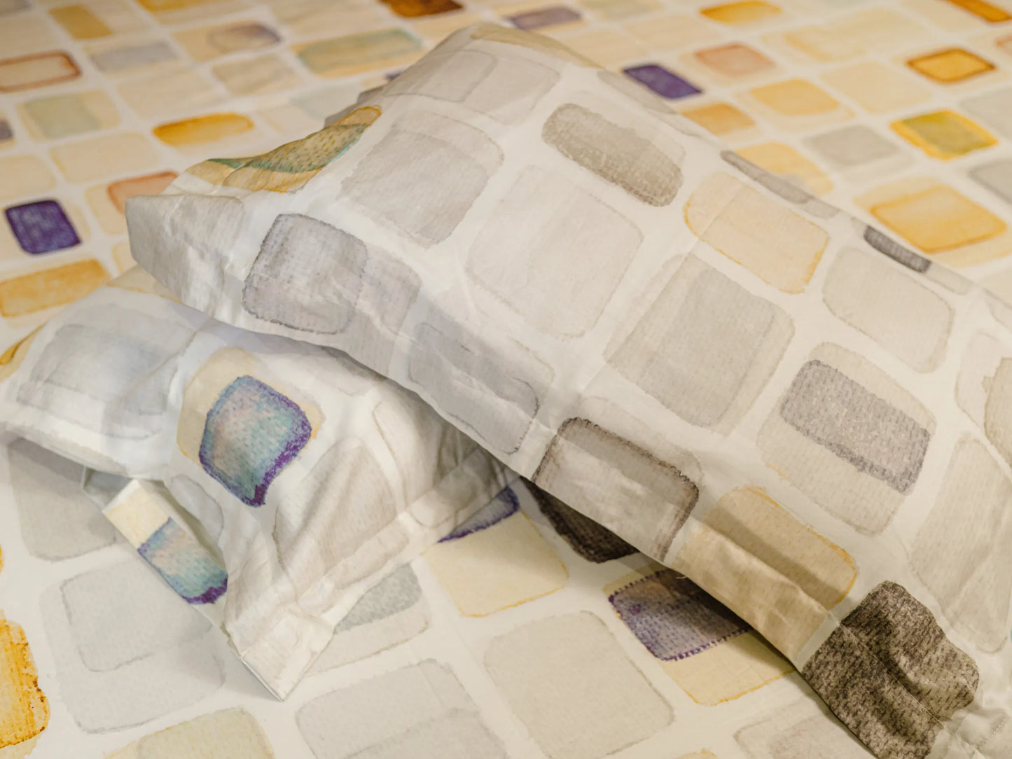 Two pillows kept over each other with Motif premium off white pillow cover and bedsheet displaying artistic geometric mosaic design with refined craftsmanship and luxury finish