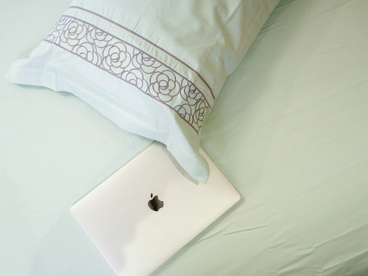 Luxury pistachio green 700 thread count organic cotton bedsheet with embroidered pillow cover styled on a super king bed with MacBook on the same bed showcasing lifestyle