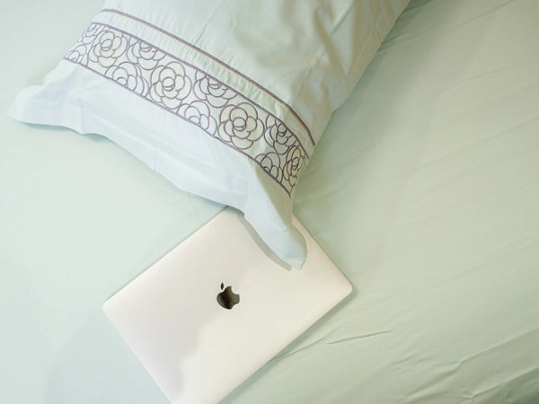 Luxury pistachio green 700 thread count organic cotton bedsheet with embroidered pillow cover styled on a super king bed with MacBook on the same bed showcasing lifestyle