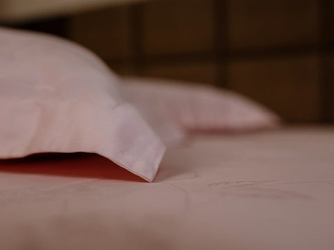 Close-up of a corner of pillow cover and bedsheet of color rose gold 1000 thread count organic cotton featuring elegant jacquard weave and soft breathable fabric
