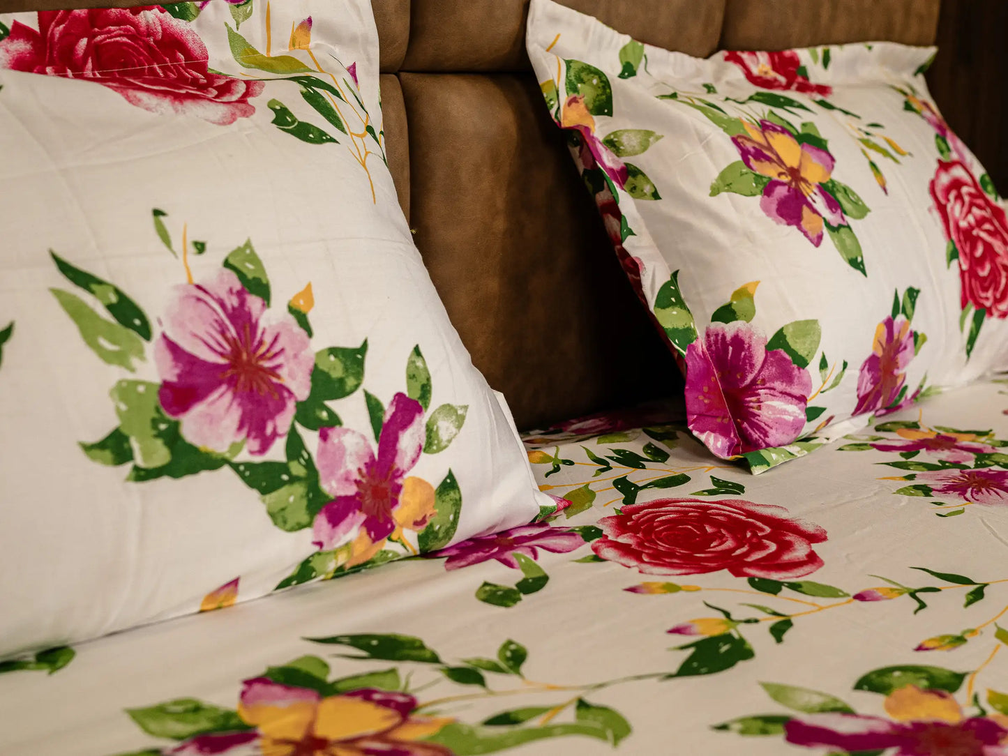 Two pillows on the corner of bed headboard on Couture white and fuchsia floral organic cotton bedsheet wrapped neatly over the luxury bed