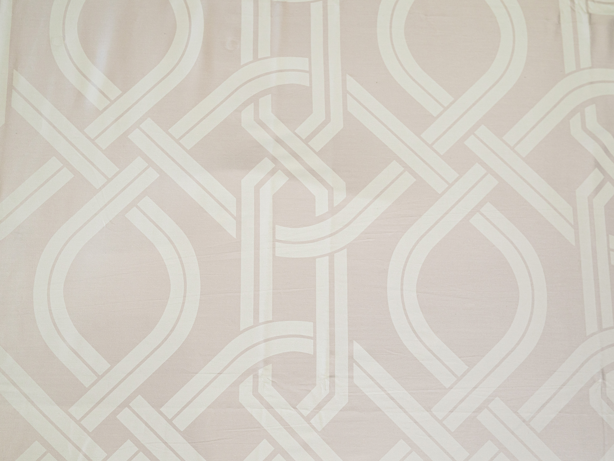 Detailed view of Chaste jacquard bedsheet fabric featuring an interlocking geometric motif in beige for a modern luxury bedroom aesthetic