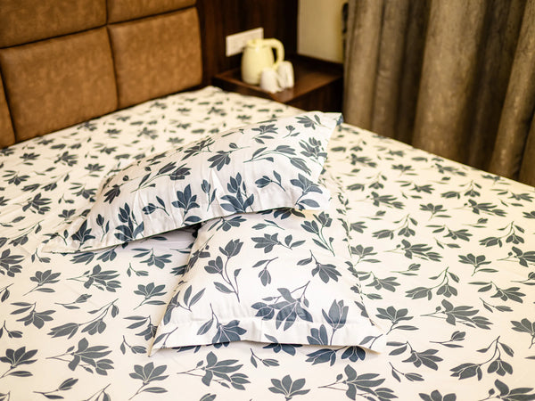 Aura luxury cotton bedsheet in bluish grey with matching pillow covers and sophisticated charcoal floral design on a modern bed