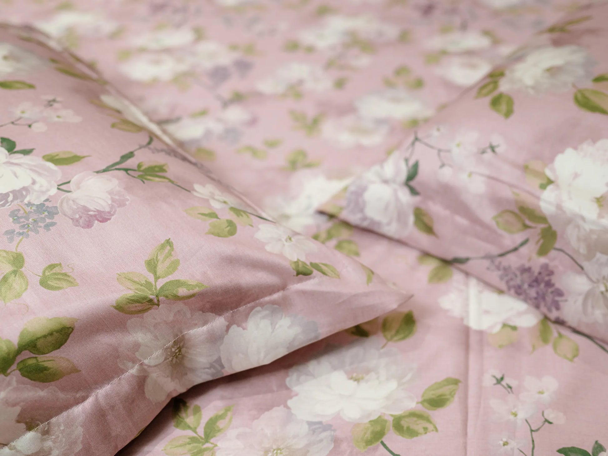 Close-up of corners of two pillows on a blush pink floral 500 thread count organic cotton bedsheet highlighting premium weave and botanical design