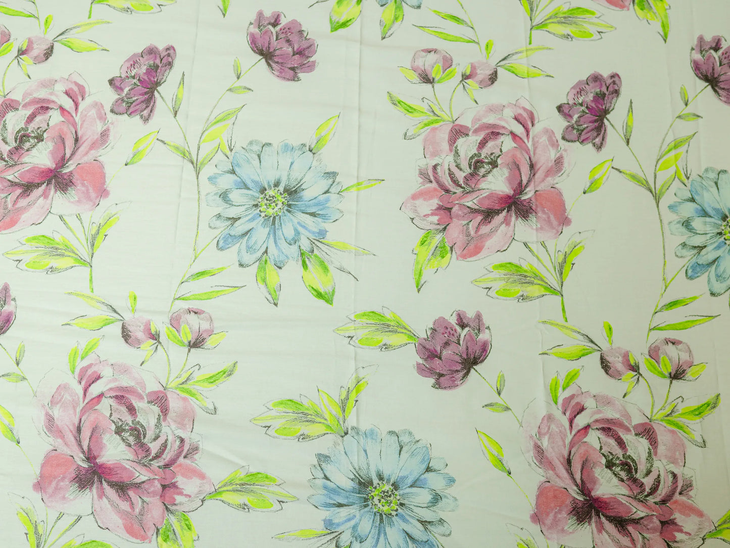 Close-up of Mosaic creamy white luxury bedsheet featuring hand-painted floral motifs with blue flowers, dusty rose blooms, and lime leaves.