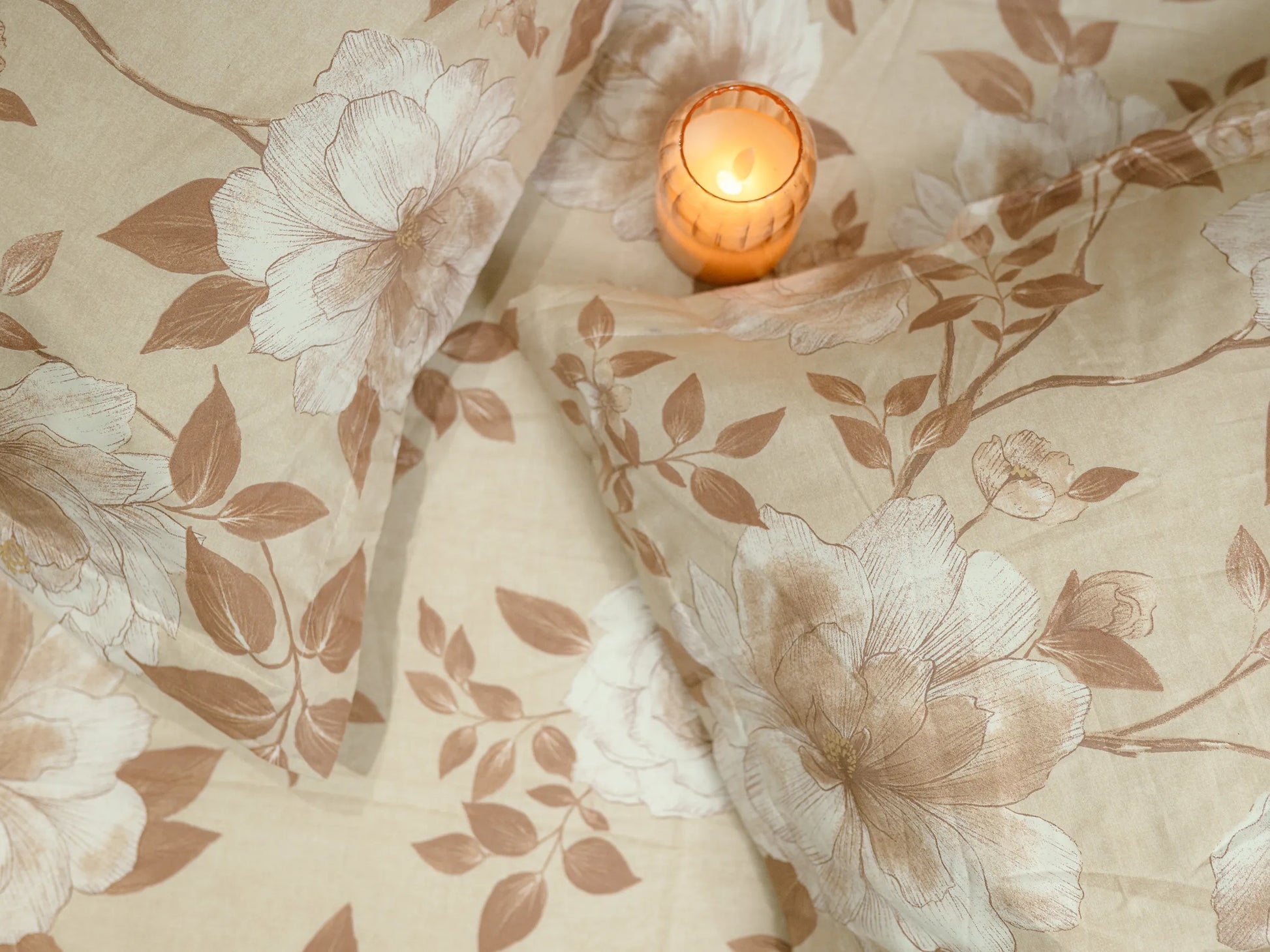 Two pillow covers kept on a bed with lifestyle candle bedside them on a luxury fawn and caramel floral organic cotton bedsheet showcasing soft 500 thread count weave and premium finish