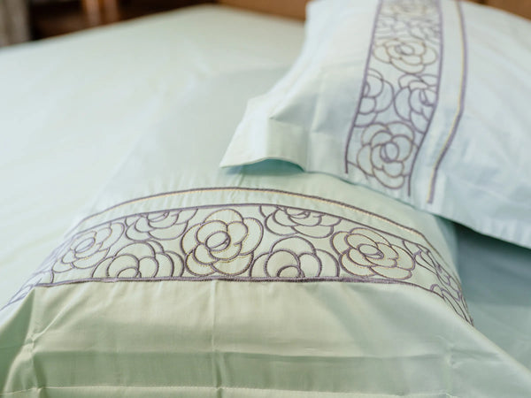 Luxury pistachio green organic cotton besheet with matching embroidered pillow covers on a super king bed